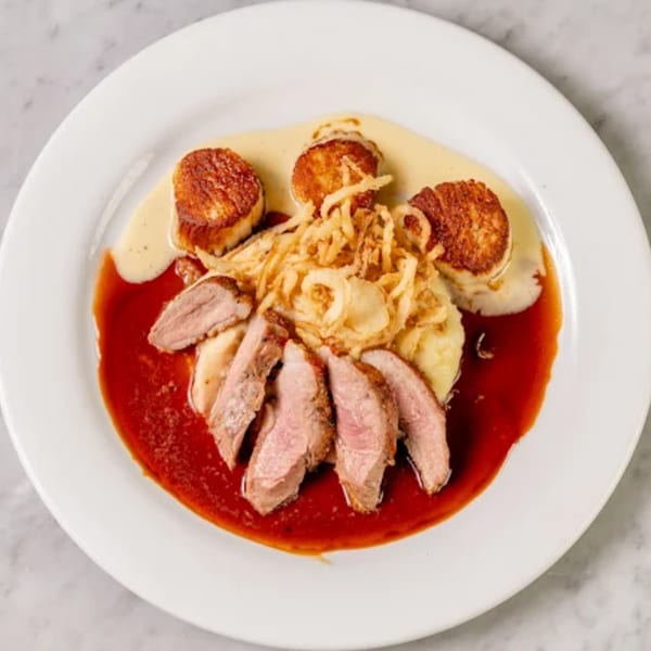 Seared scallops, sliced duck, mashed potatoes, and crispy onions with red and cream sauces.