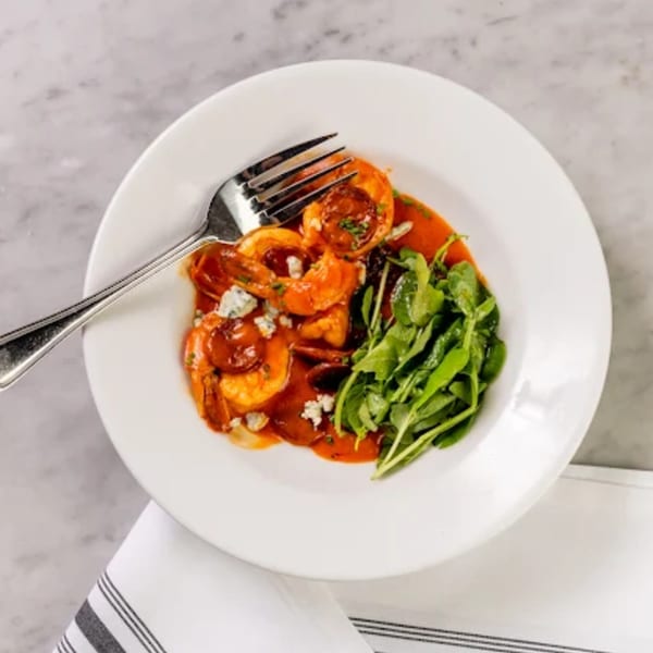 Shrimp and chorizo in a red sauce with blue cheese crumbles and a side of arugula.