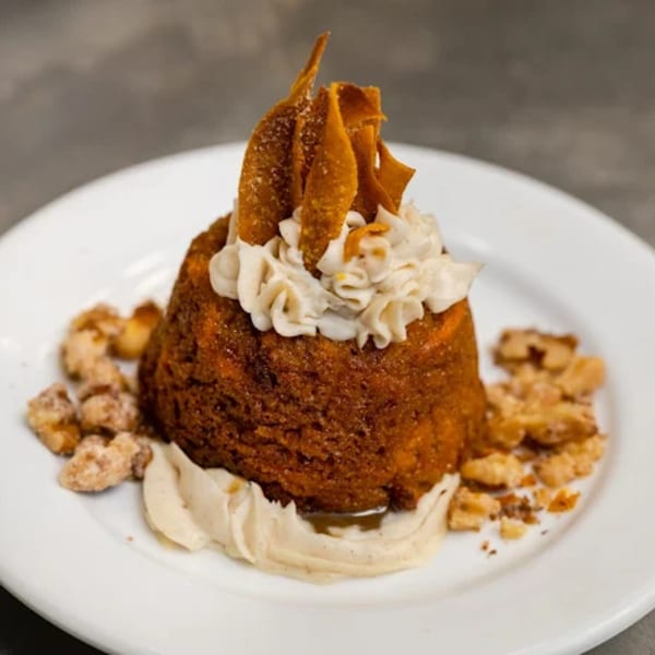A Noble Lion dessert with a bundt cake, cream cheese frosting, and candied nuts on a white plate.