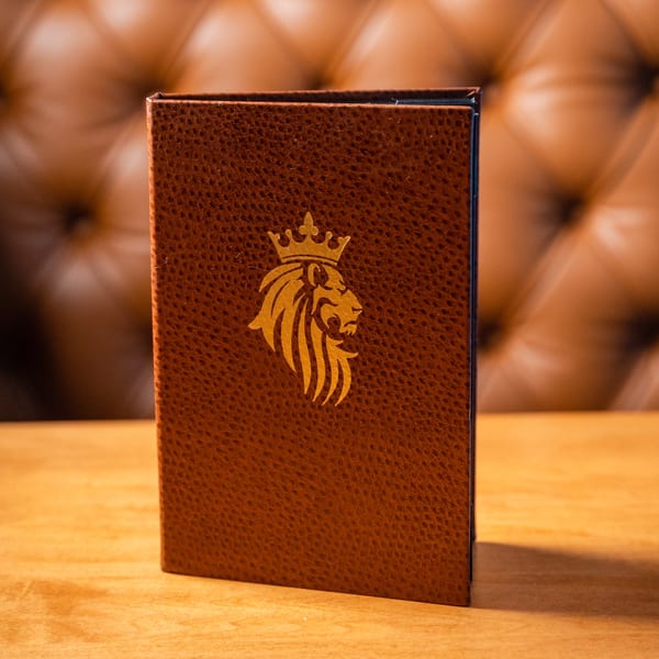 Brown leather menu with a gold lion and crown logo on a wooden table.