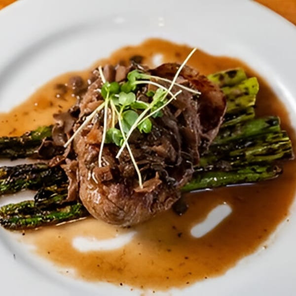 The Noble Lion's steak with grilled asparagus, mushrooms, and microgreens, drizzled with sauce.