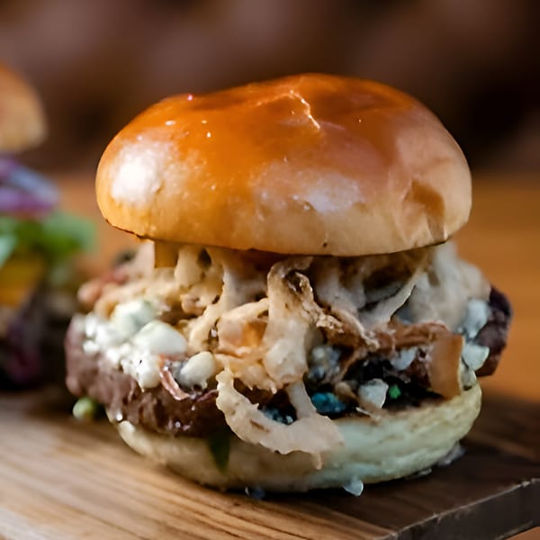 Close-up of a gourmet burger with crispy fried onions and blue cheese crumbles on a wooden board.