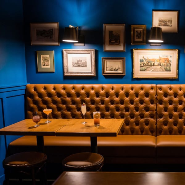 Cozy booth seating with brown tufted leather, wooden tables, cocktails, and framed art on a blue wall.